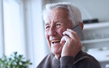 Older man talking on a cell phone in his home utilizing VoIP, a Viasat internet add-on